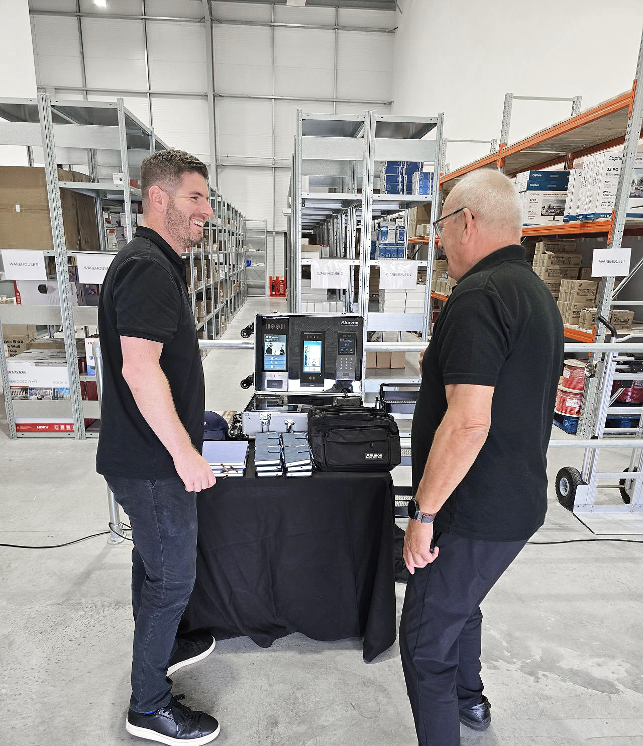CIE Group team member speaking with a visitor beside an Akuvox product display in a warehouse setting
