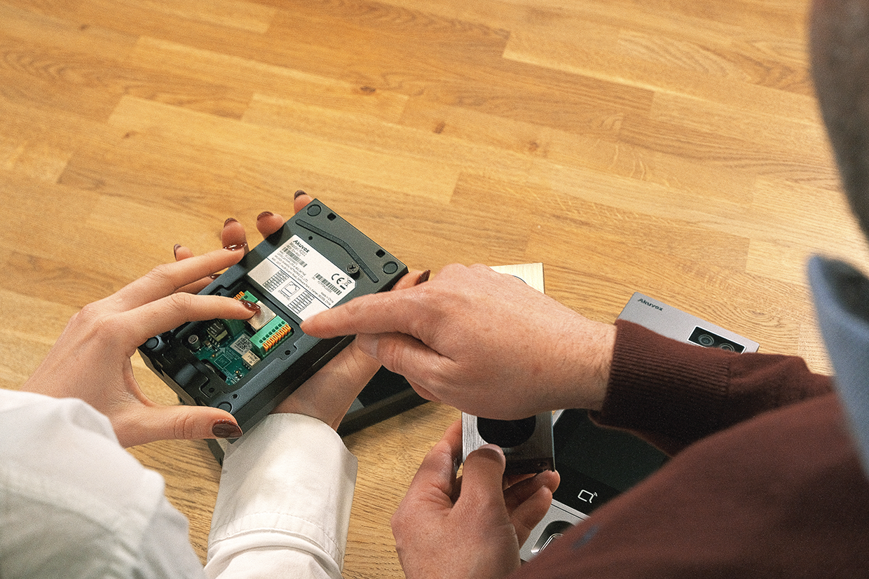 Two people examining the internal components of an Akuvox access control device alongside other intercom hardware
