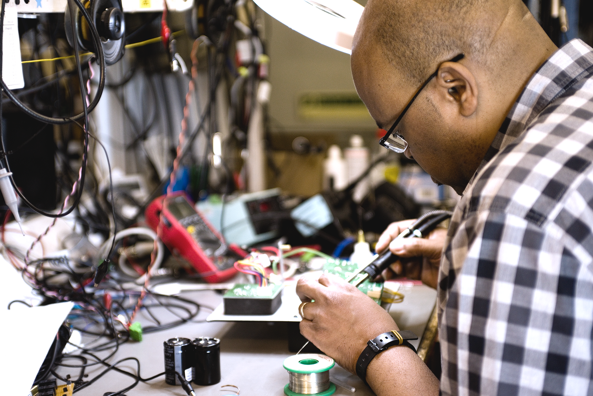 Engineer soldering and testing an electronic circuit board at a technical workbench