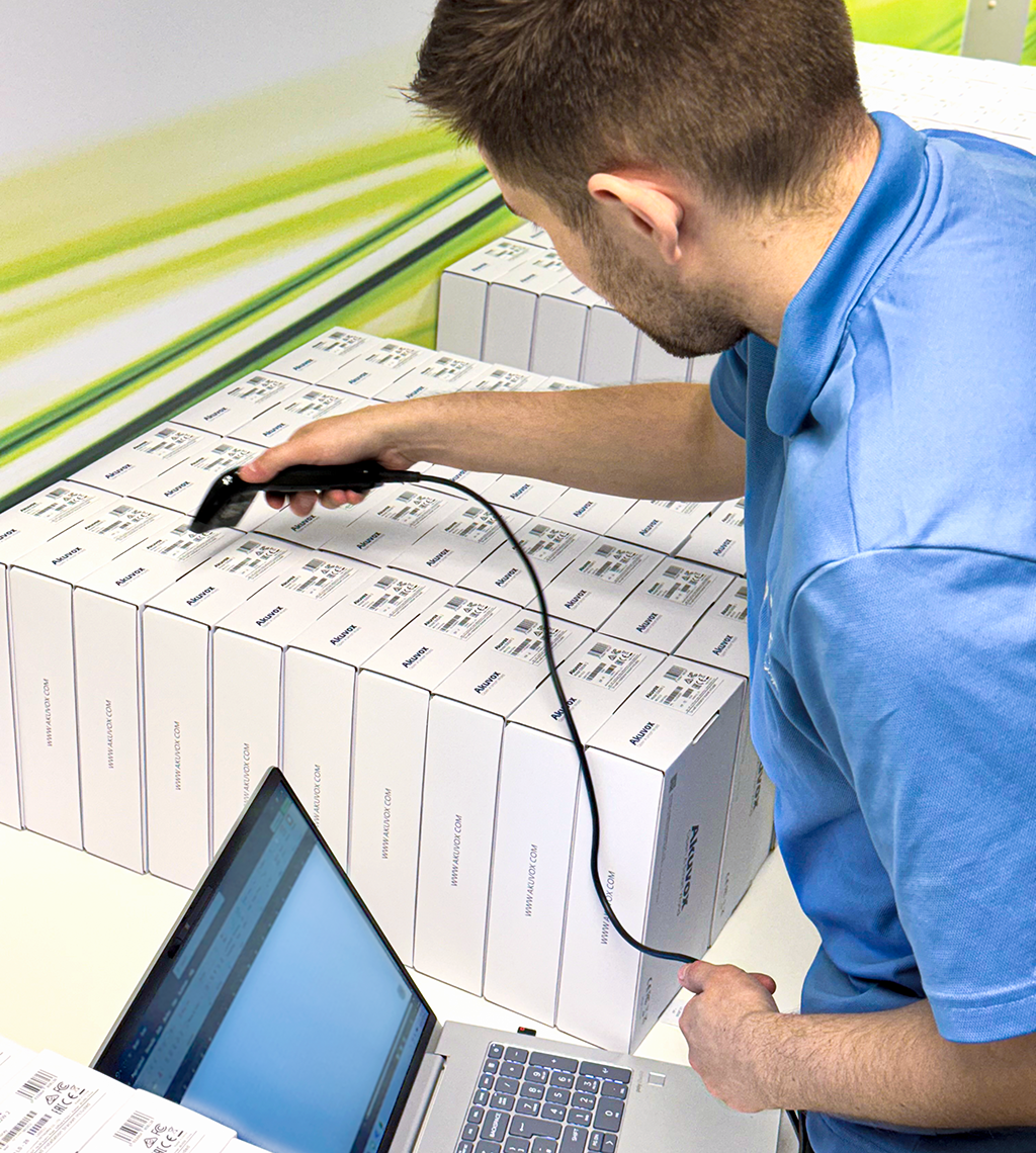 Technician scanning barcode labels on boxed Akuvox products while recording inventory on a laptop