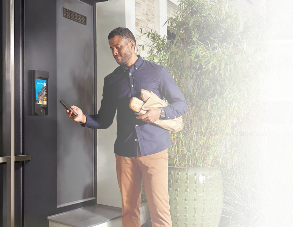 Man using a smartphone to access a building entrance with a 2N smart intercom while carrying groceries
