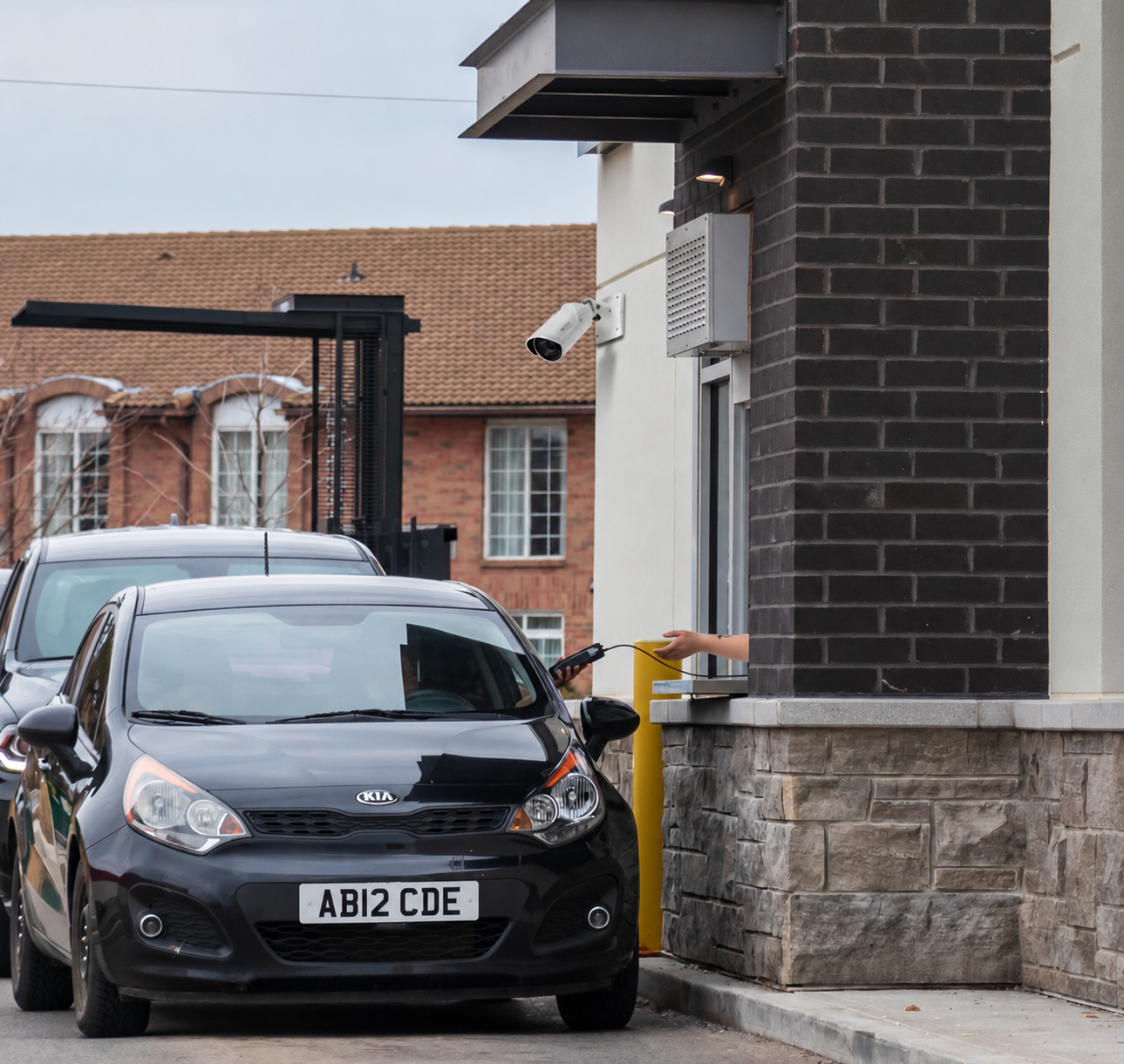 Drive-through service window with a security camera overlooking a car as an item is handed through the window
