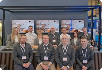 CIE Group team members posing together at a trade show stand with presentation screens in the background