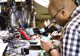 Engineer soldering and testing an electronic circuit board at a technical workbench