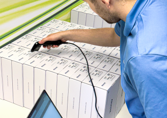Technician scanning barcode labels on boxed Akuvox products while recording inventory on a laptop